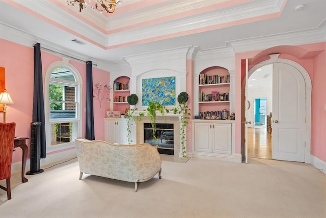 living room featuring built in features, ornamental molding, a tray ceiling, light carpet, and a fireplace