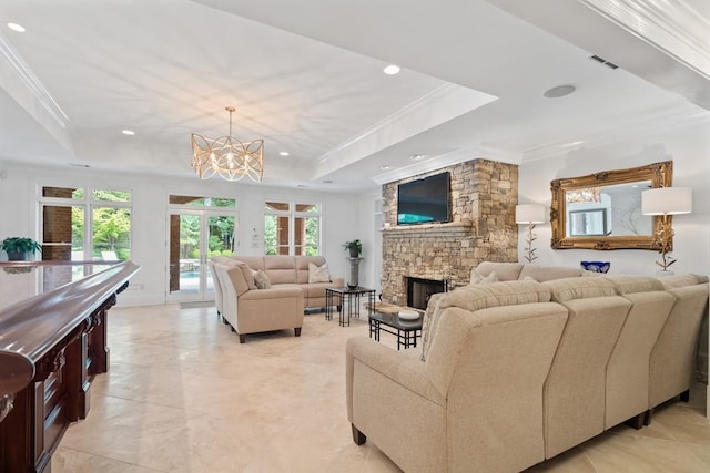 living room with an inviting chandelier, a raised ceiling, ornamental molding, and a stone fireplace