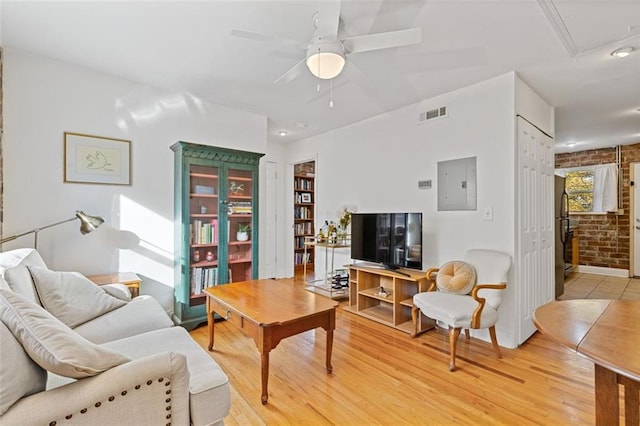 living room featuring ceiling fan, light hardwood / wood-style floors, brick wall, and electric panel