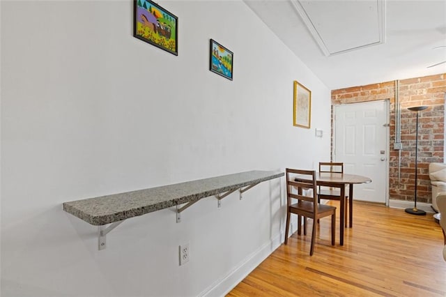 dining area with brick wall and light wood-type flooring