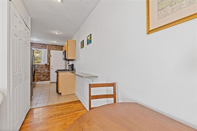 interior space featuring appliances with stainless steel finishes, light brown cabinets, brick wall, and light hardwood / wood-style flooring