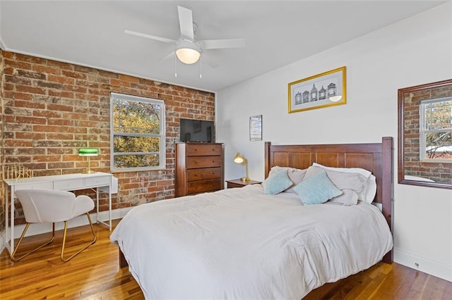 bedroom featuring wood-type flooring, ceiling fan, and brick wall