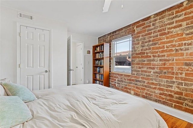 bedroom featuring ceiling fan, wood-type flooring, and brick wall