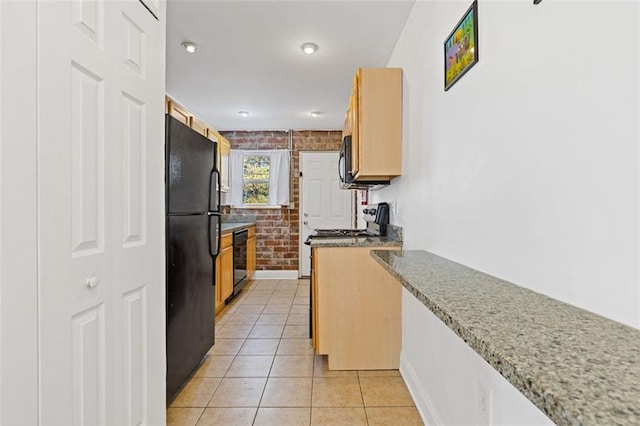 kitchen with brick wall, light tile patterned floors, light stone countertops, and black appliances