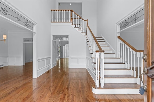 stairway featuring visible vents, wainscoting, wood finished floors, a decorative wall, and a high ceiling