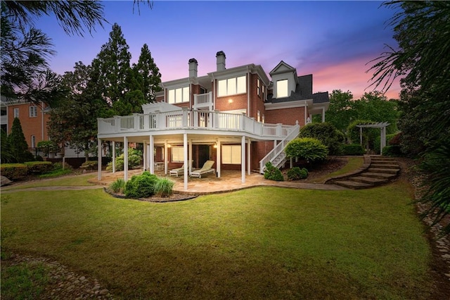 rear view of property with a deck, a patio, a chimney, brick siding, and stairway