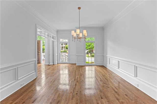 unfurnished dining area featuring a healthy amount of sunlight, crown molding, a decorative wall, and a notable chandelier