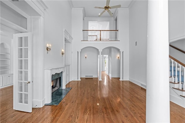 unfurnished living room featuring ceiling fan, decorative columns, crown molding, arched walkways, and wood finished floors