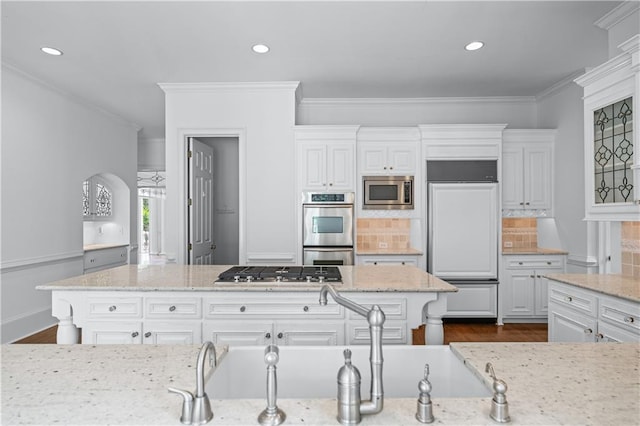 kitchen featuring light stone counters, built in appliances, backsplash, and white cabinets