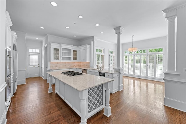 kitchen with a peninsula, decorative columns, ornamental molding, and stainless steel gas stovetop