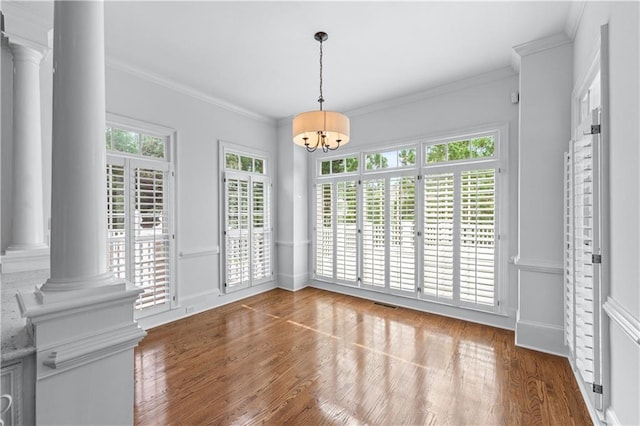 unfurnished dining area with crown molding, ornate columns, wood finished floors, and a chandelier