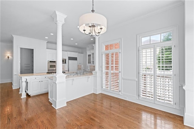 kitchen with ornamental molding, decorative columns, a peninsula, oven, and white cabinets