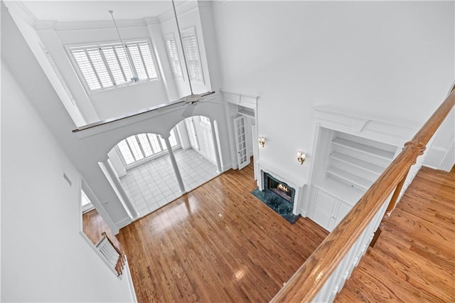 interior space with ornamental molding, wood finished floors, a high ceiling, a lit fireplace, and plenty of natural light