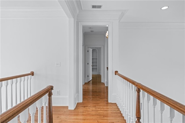 hall with visible vents, crown molding, baseboards, an upstairs landing, and light wood-style floors