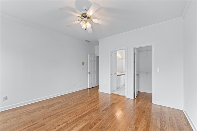 unfurnished bedroom featuring ornamental molding, light wood-type flooring, ensuite bath, and a spacious closet