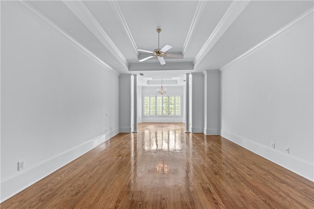 spare room with a raised ceiling, baseboards, wood finished floors, ornate columns, and ornamental molding