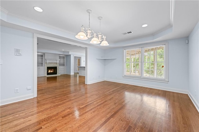 unfurnished living room featuring ornamental molding, a notable chandelier, a tray ceiling, and visible vents