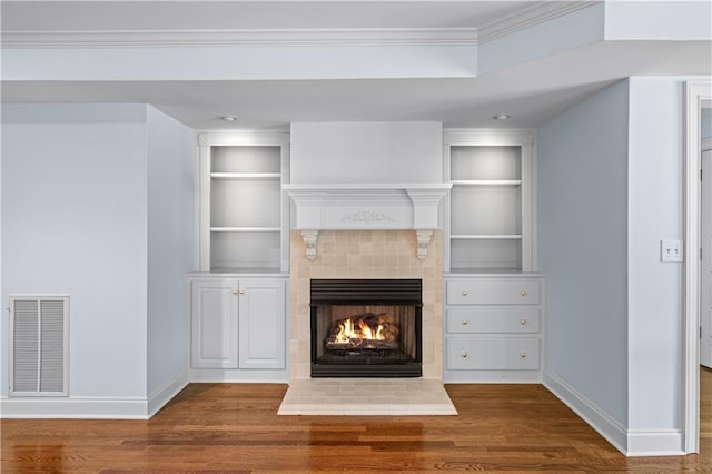 unfurnished living room featuring built in shelves, baseboards, wood finished floors, and visible vents