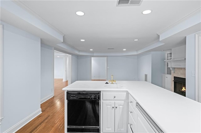 kitchen with visible vents, light wood-style floors, black dishwasher, a tiled fireplace, and a sink