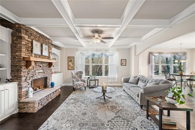 living room with a stone fireplace, plenty of natural light, dark wood-type flooring, and beamed ceiling