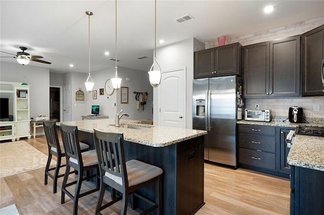 kitchen with sink, dark brown cabinetry, stainless steel refrigerator with ice dispenser, and an island with sink