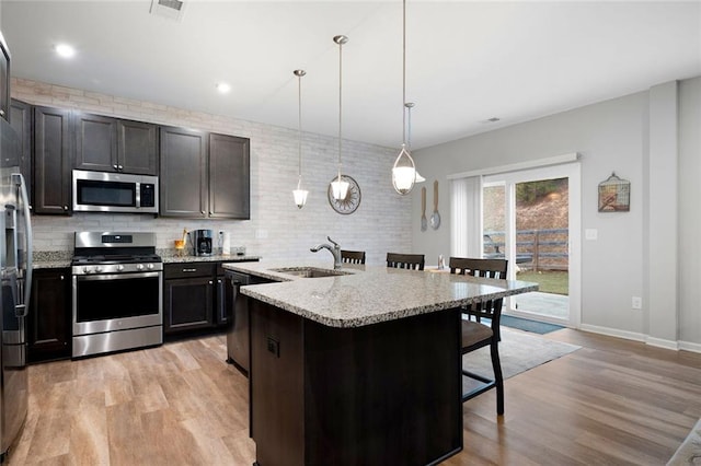 kitchen with sink, an island with sink, pendant lighting, a breakfast bar, and appliances with stainless steel finishes