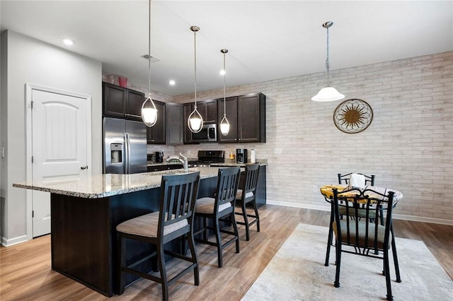 kitchen with hanging light fixtures, light hardwood / wood-style floors, stainless steel appliances, and brick wall