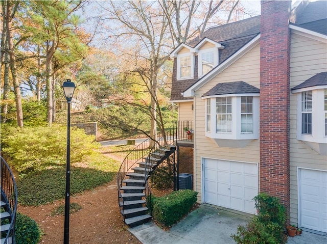 view of home's exterior with a garage, driveway, roof with shingles, stairs, and central AC