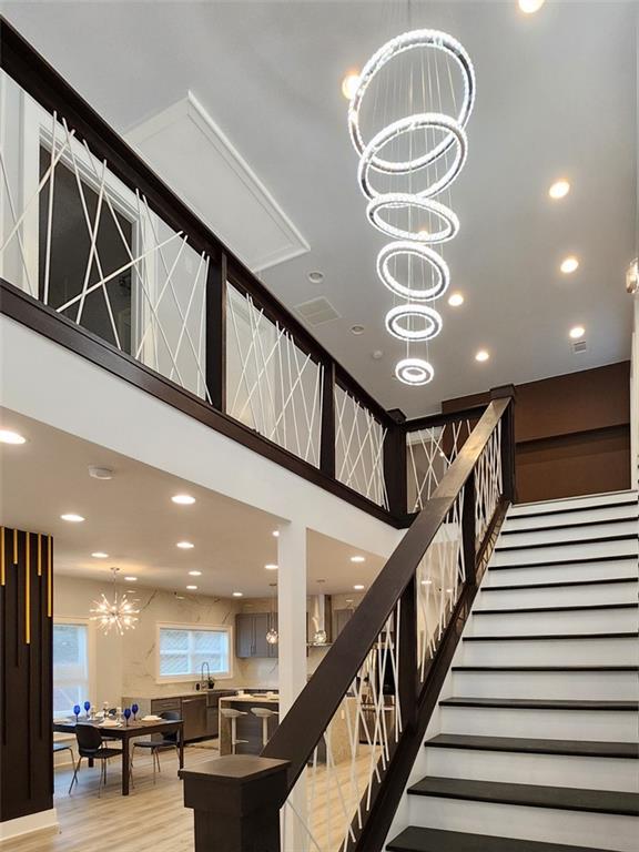 stairway with a high ceiling, an inviting chandelier, sink, and light hardwood / wood-style flooring