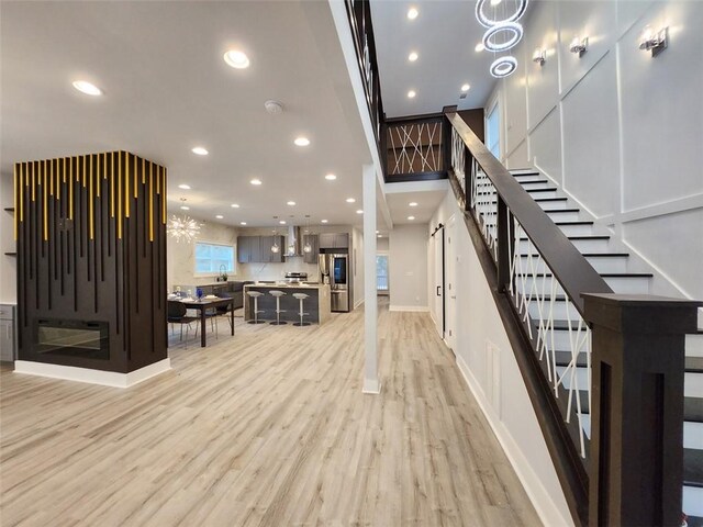 staircase featuring a barn door, a chandelier, sink, and light hardwood / wood-style flooring