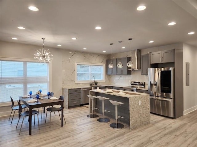 kitchen with a chandelier, stainless steel appliances, a kitchen island, a kitchen bar, and wall chimney exhaust hood