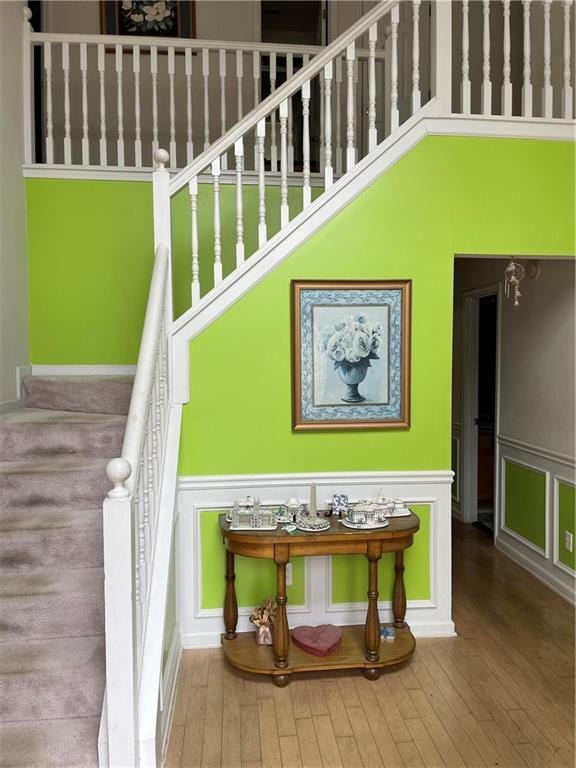 stairway featuring hardwood / wood-style floors, wainscoting, a towering ceiling, and a decorative wall