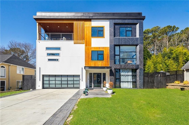 contemporary home featuring an attached garage, fence, a front yard, stucco siding, and driveway