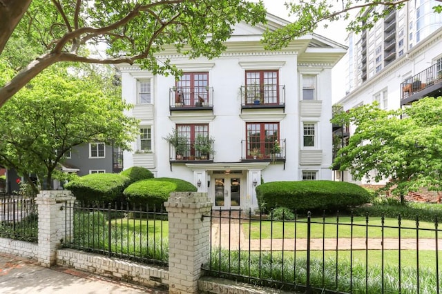 neoclassical / greek revival house with a fenced front yard, french doors, a balcony, and stucco siding