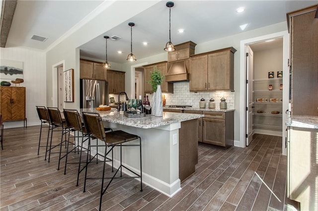 kitchen featuring pendant lighting, a kitchen island with sink, light stone countertops, appliances with stainless steel finishes, and a breakfast bar area