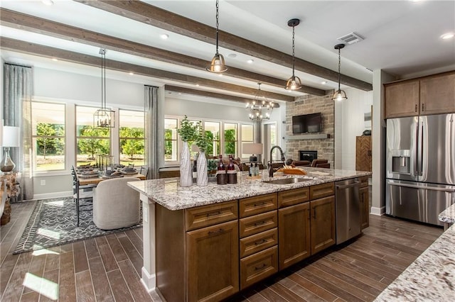 kitchen featuring beam ceiling, sink, an island with sink, pendant lighting, and appliances with stainless steel finishes