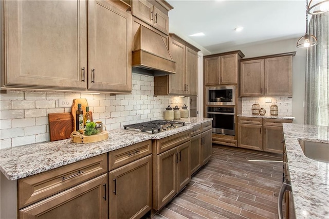 kitchen featuring light stone countertops, stainless steel appliances, pendant lighting, decorative backsplash, and custom exhaust hood