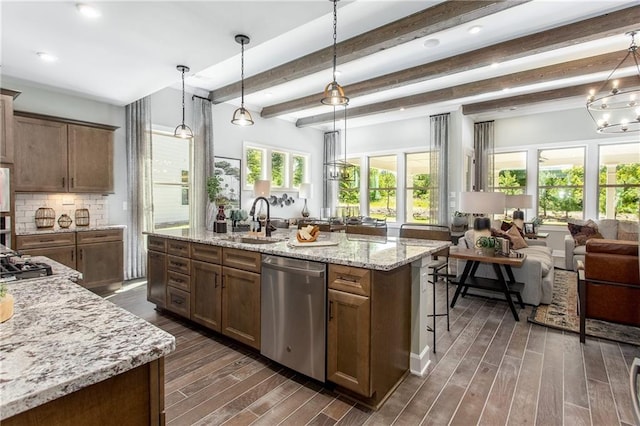 kitchen featuring dishwasher, sink, beamed ceiling, an island with sink, and decorative light fixtures