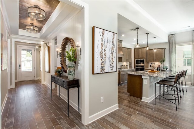 kitchen with hanging light fixtures, light stone counters, dark hardwood / wood-style flooring, a tray ceiling, and a breakfast bar