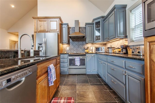 kitchen featuring sink, wall chimney range hood, appliances with stainless steel finishes, dark stone counters, and decorative backsplash