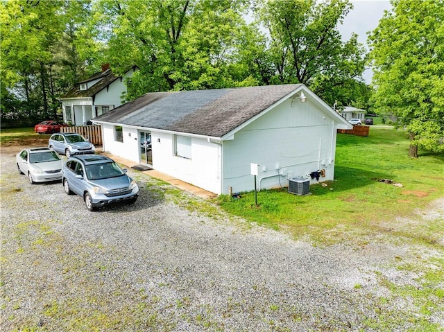 view of side of home featuring a shingled roof, driveway, a lawn, and view of wooded area