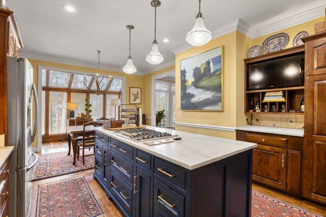 kitchen with crown molding, stainless steel appliances, a kitchen island, decorative light fixtures, and light wood-type flooring