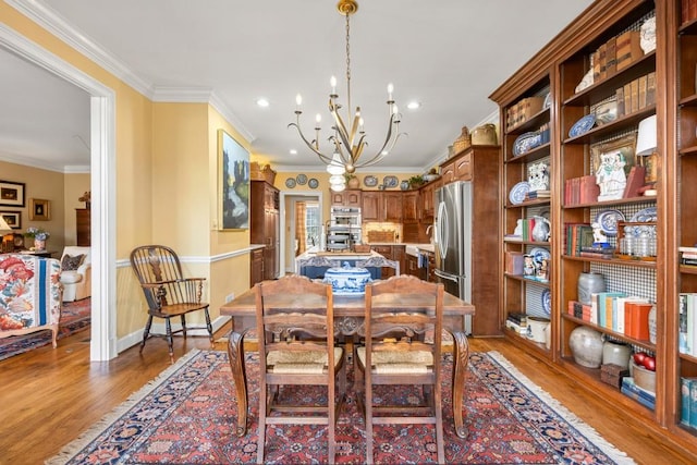 dining area with wood-type flooring, ornamental molding, and an inviting chandelier