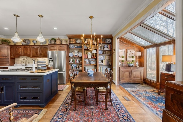 kitchen with crown molding, appliances with stainless steel finishes, pendant lighting, and light hardwood / wood-style flooring