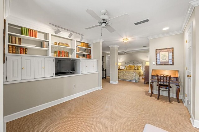 carpeted bedroom featuring crown molding, rail lighting, ceiling fan, and ornate columns