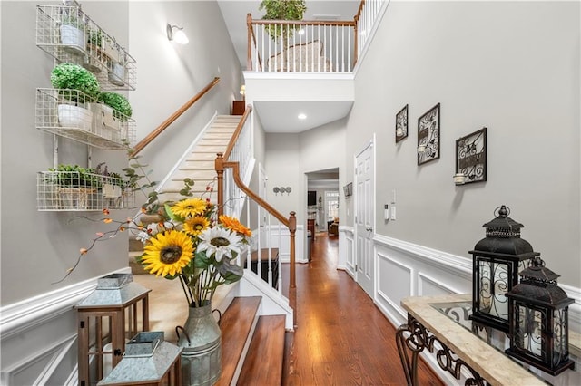 foyer entrance with a towering ceiling, a wainscoted wall, wood finished floors, stairs, and a decorative wall