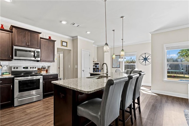 kitchen with a kitchen bar, dark hardwood / wood-style flooring, stainless steel appliances, decorative light fixtures, and a center island with sink