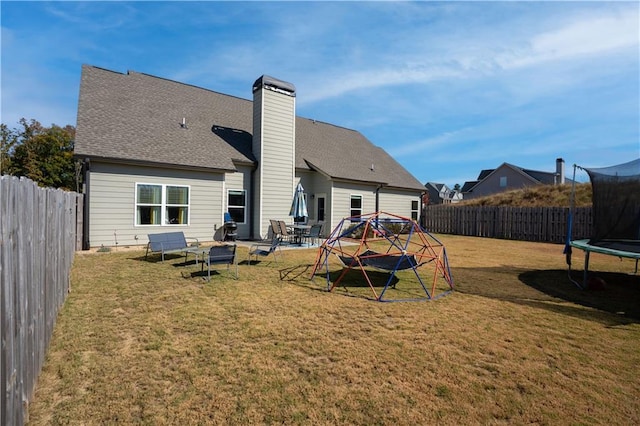 rear view of property featuring a patio area, a yard, and a trampoline