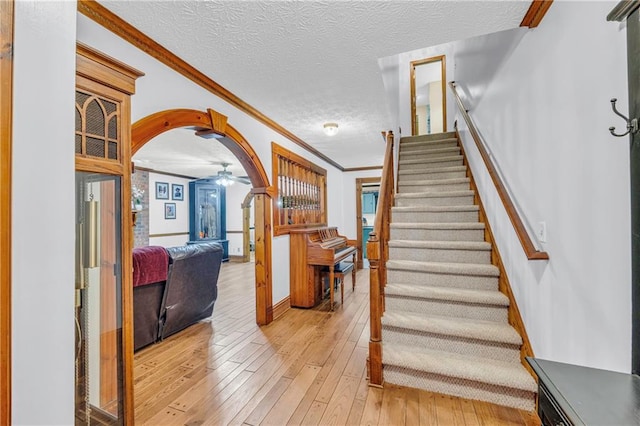 staircase with ceiling fan, ornamental molding, wood-type flooring, and a textured ceiling