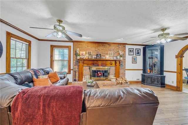 living room featuring a fireplace, a textured ceiling, ceiling fan, and light hardwood / wood-style floors